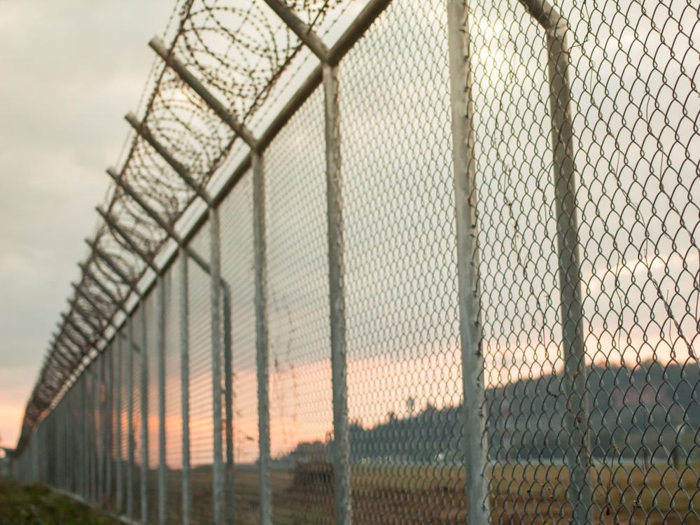 Photo of a tall security chain link fence with barbed wire